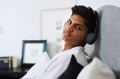 Buy stock photo Cropped shot of a young man listening to music through his headphones while relaxing at home