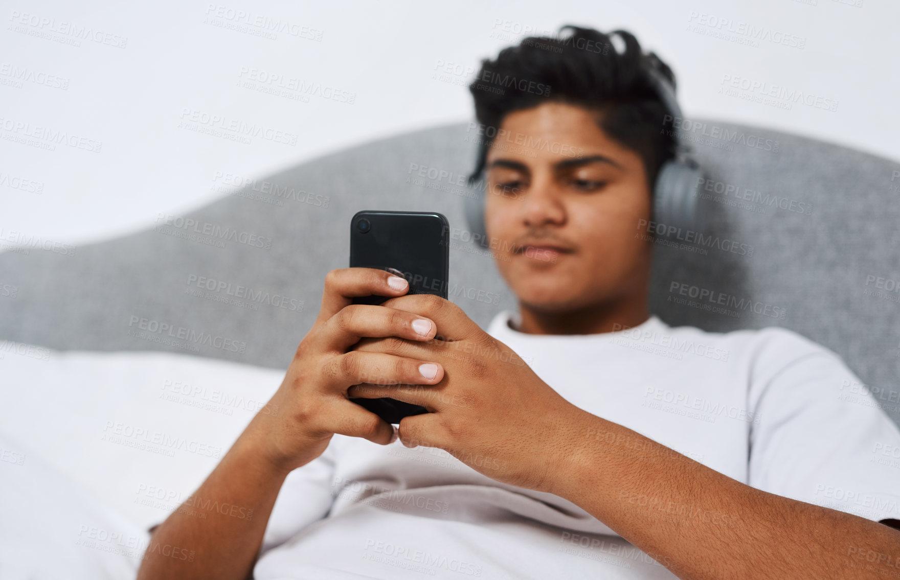 Buy stock photo Cropped shot of a young man using his cellphone while listening to music through his headphones