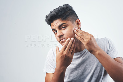 Buy stock photo Studio shot of a young man inspecting his skin while sitting against a white background