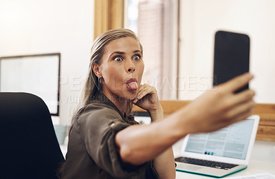 Buy stock photo Phone selfie with a playful business woman having fun, being goofy and joking while working in her office. Young female sticking out her tongue and making a face at work while feeling carefree