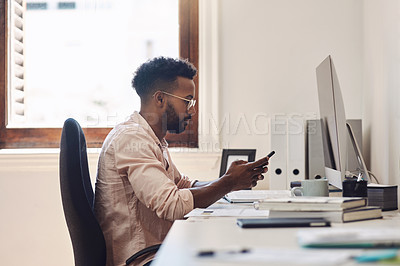 Buy stock photo Shot of a young businessman using a cellphone while working in an office