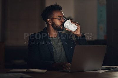 Buy stock photo Shot of a young businessman having coffee and using a laptop during a late night at work