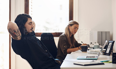 Buy stock photo Shot of a young businessman sitting with his hands behind his head while working in an office