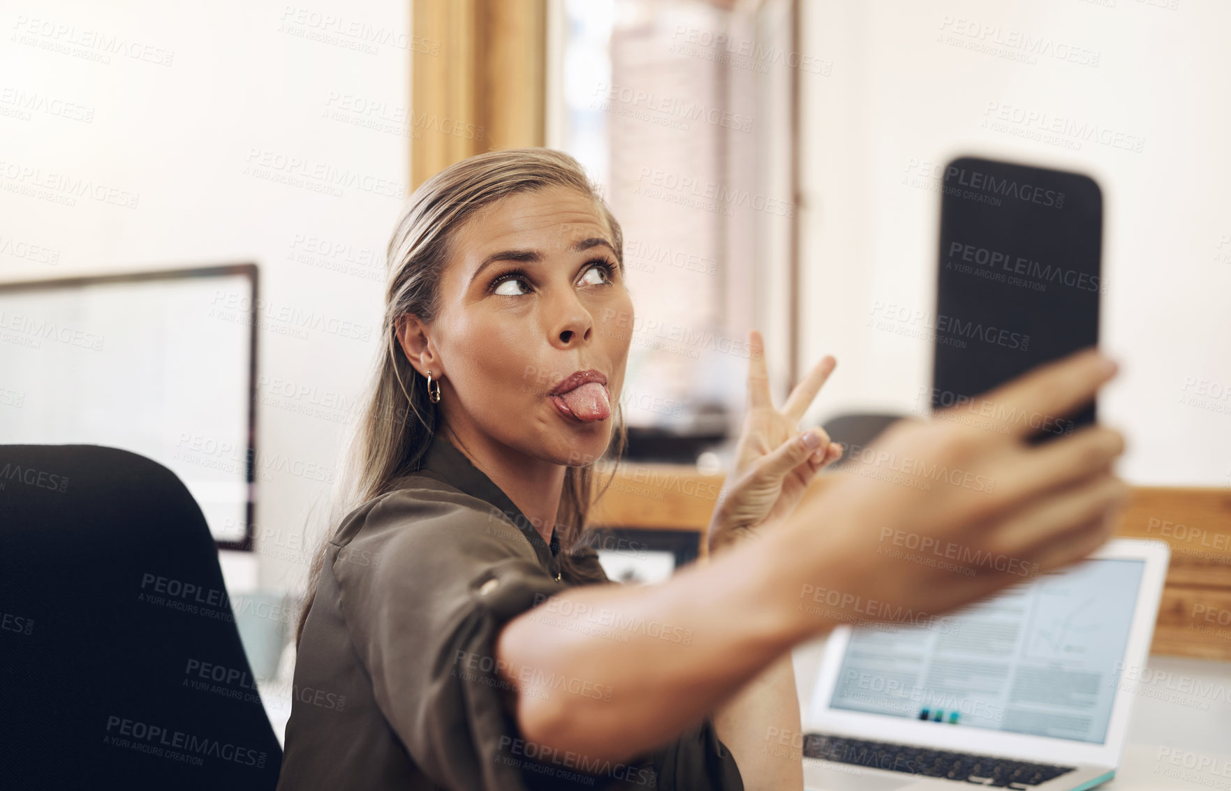 Buy stock photo Shot of a young businesswoman sticking out her tongue while taking selfies in an office