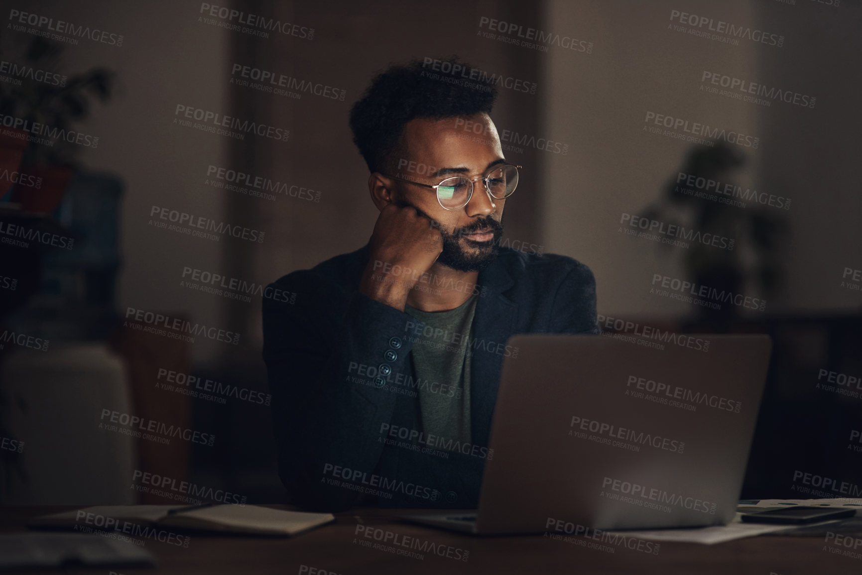 Buy stock photo Shot of a young businessman looking worn out while using a laptop during a late night at work