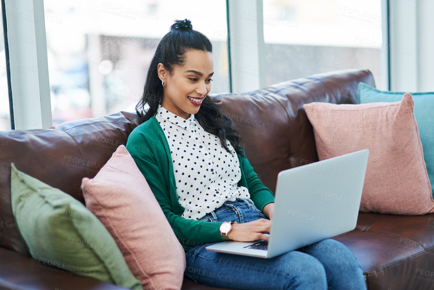 Buy stock photo Shot of a young woman using a laptop while relaxing on a sofa