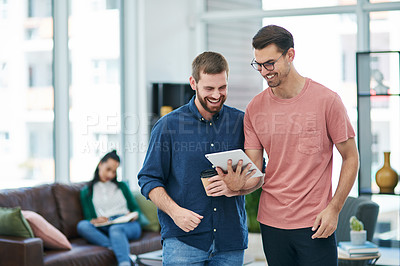 Buy stock photo Shot of two young businessmen using a digital tablet together in a modern office