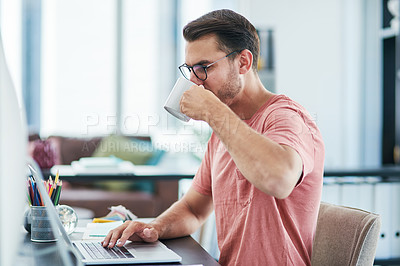 Buy stock photo Shot of a young businessman having coffee while using a computer in a modern office