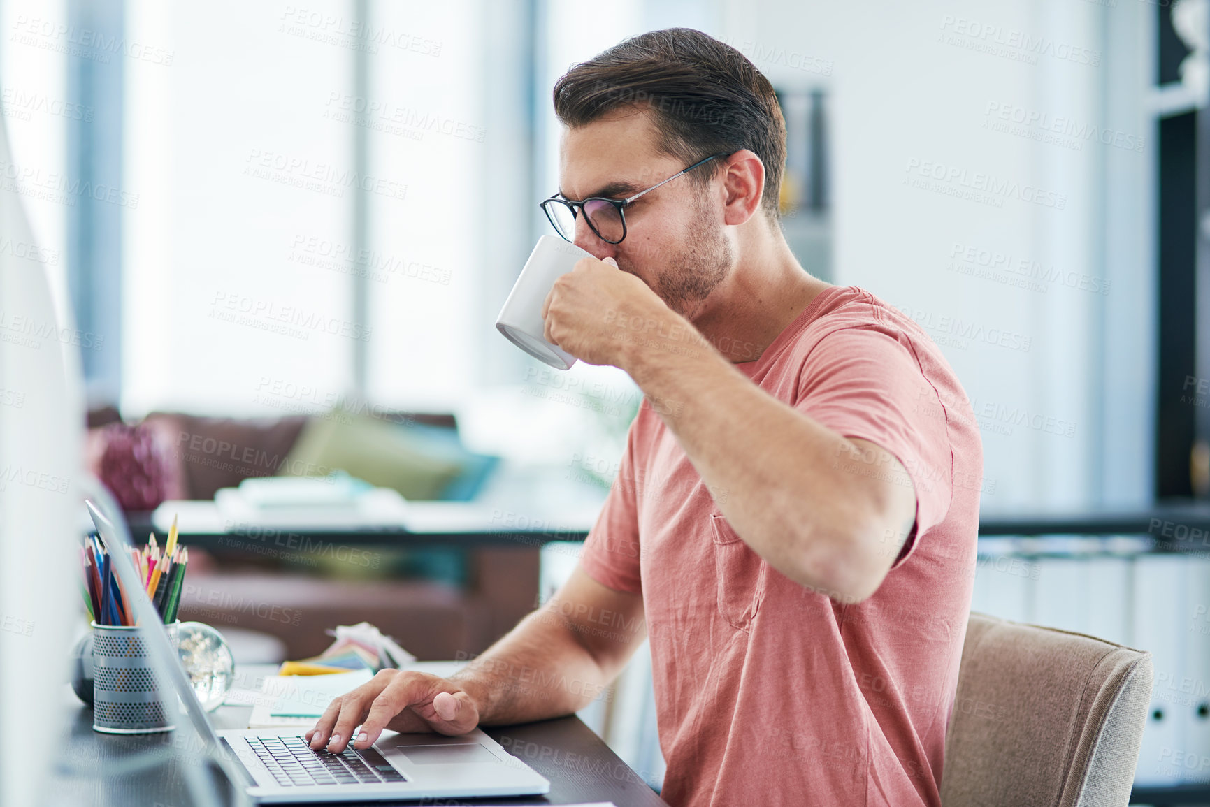Buy stock photo Shot of a young businessman having coffee while using a computer in a modern office