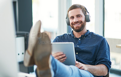 Buy stock photo Shot of a young businessman using a digital tablet and headphones in a modern office