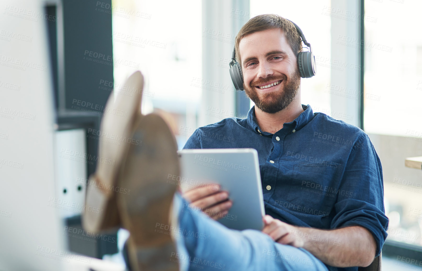 Buy stock photo Shot of a young businessman using a digital tablet and headphones in a modern office