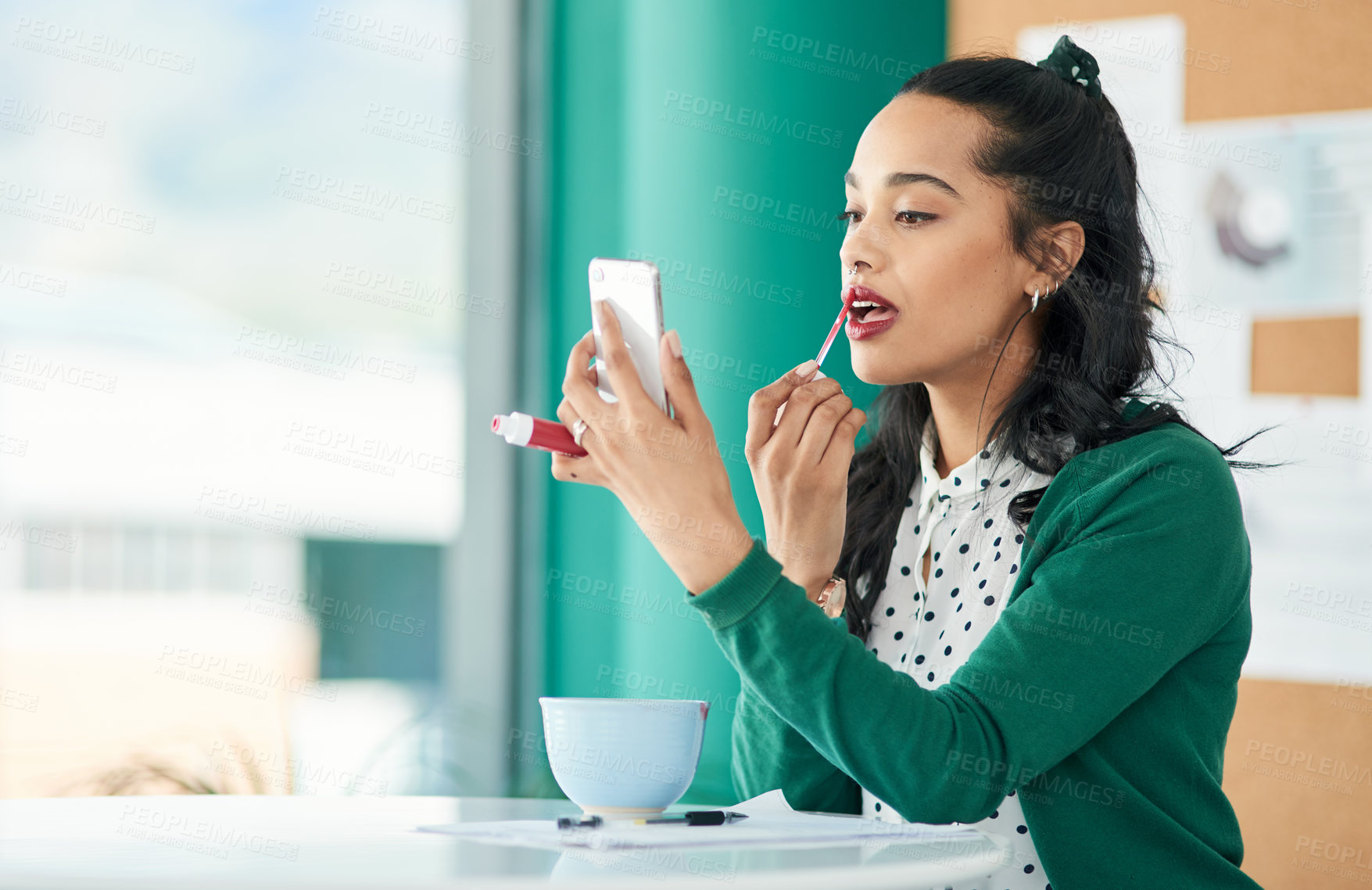 Buy stock photo Shot of a young businesswoman applying lipstick using a smartphone in a modern office
