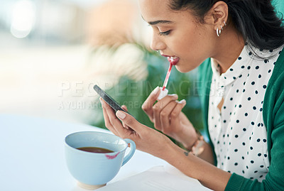 Buy stock photo Shot of a young businesswoman applying lipstick using a smartphone with a smudge of it on a cup at work