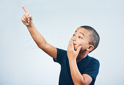 Buy stock photo Studio shot of a cute little boy pointing and looking amazed against a grey background