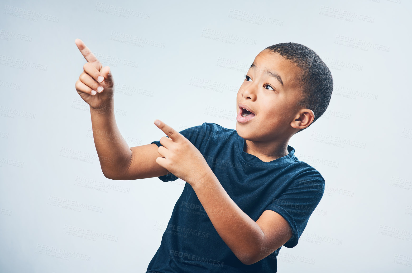 Buy stock photo Studio shot of a cute little boy pointing and looking amazed against a grey background