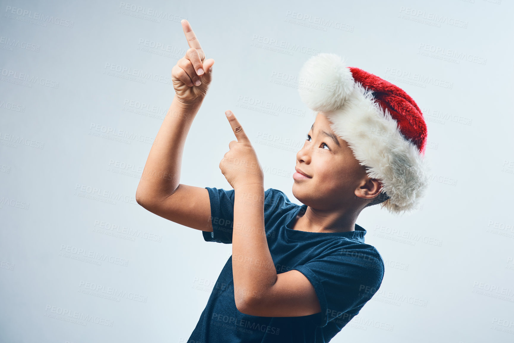 Buy stock photo Studio shot of a cute little boy wearing a Santa Claus hat and pointing against a grey background
