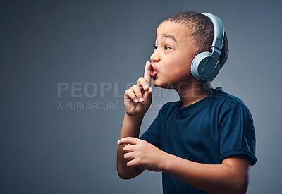 Buy stock photo Studio shot of a cute little boy using headphones and putting his finger on his lips against a grey background