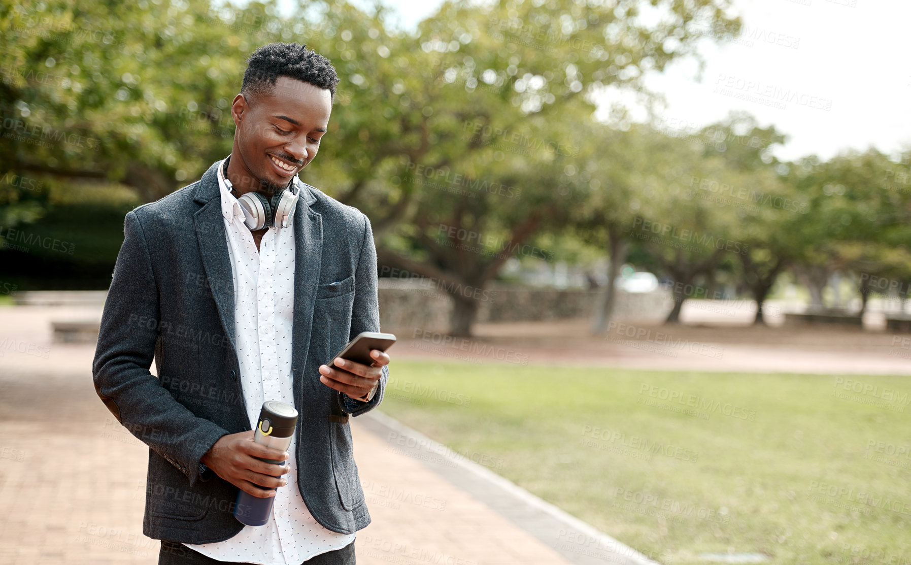 Buy stock photo Young, cool smiling businessman on a phone having a walk in the park outside in nature. Happy man texting, chatting or reading messages on a smartphone outdoors on a break from work, over copy space.