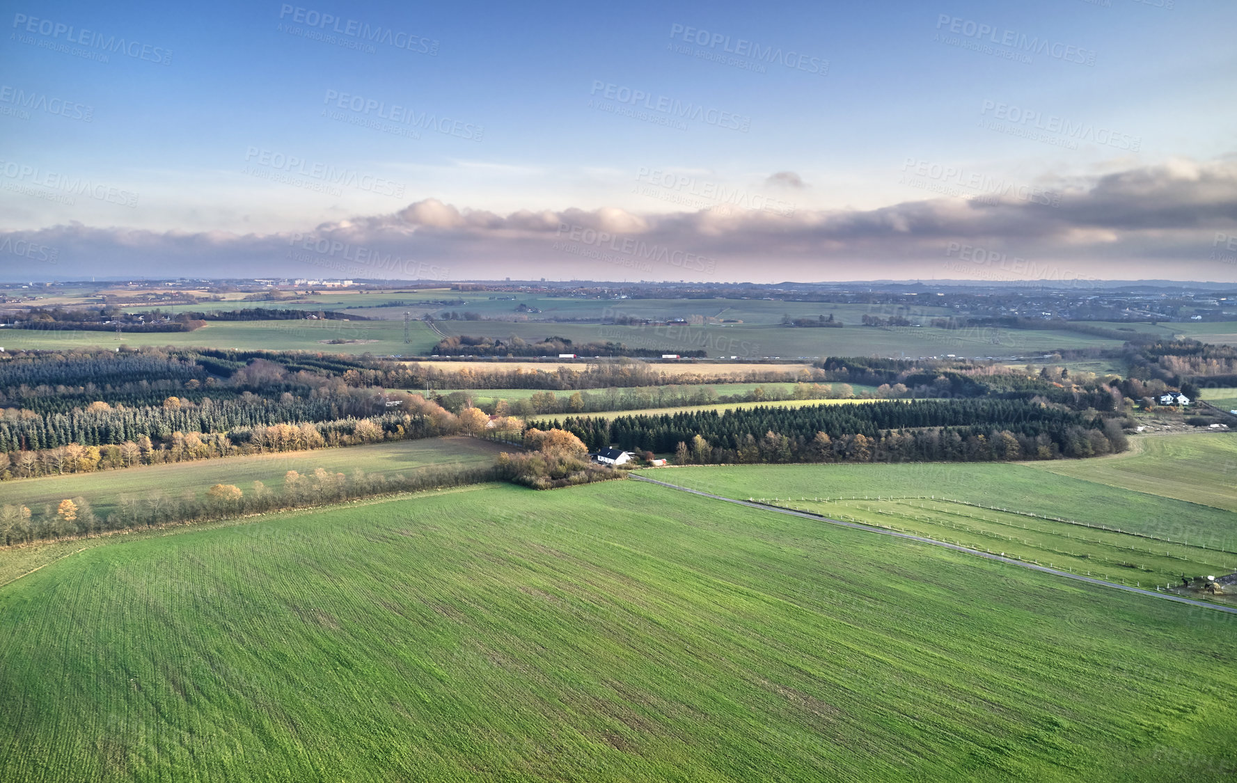 Buy stock photo Serene landscape of endless grass fields with trees in the peaceful and quiet countryside against vibrant blue horizon with copy space. Aerial view of rural farm land on a cloudy summer day in Europe