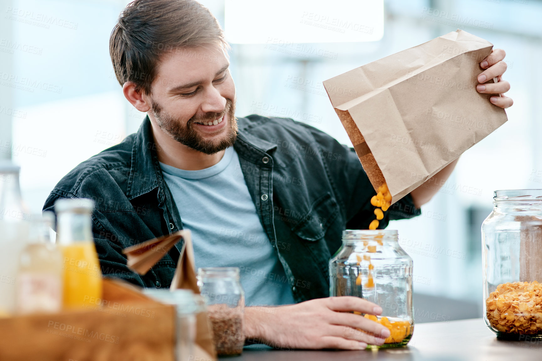 Buy stock photo Shot of a young man packing his groceries into glass containers after returning home from the store