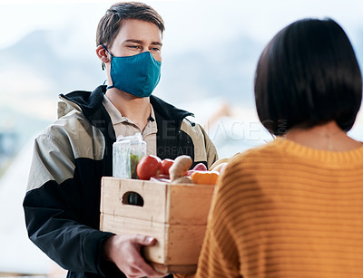 Buy stock photo Shot of a masked young man delivery fresh fruit and vegetables to a woman at home