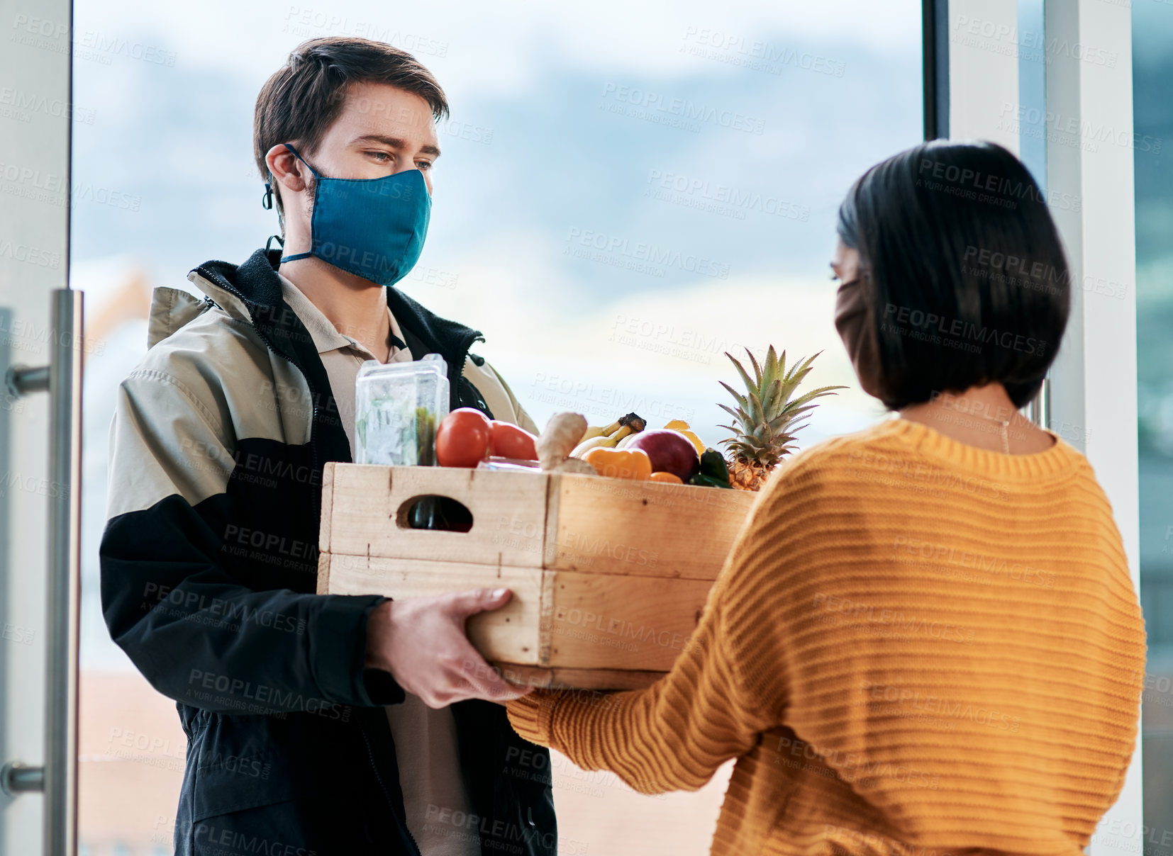 Buy stock photo Shot of a masked young man delivery fresh fruit and vegetables to a woman at home