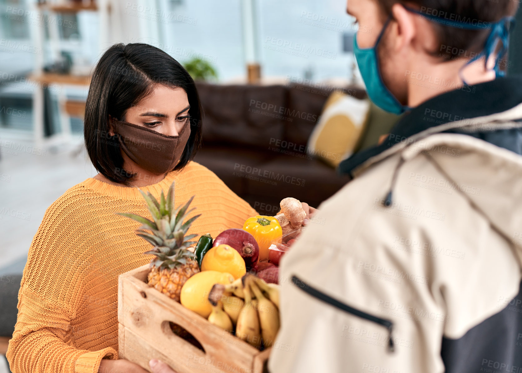 Buy stock photo Shot of a masked young woman receiving a delivery of fresh fruit and vegetables at home