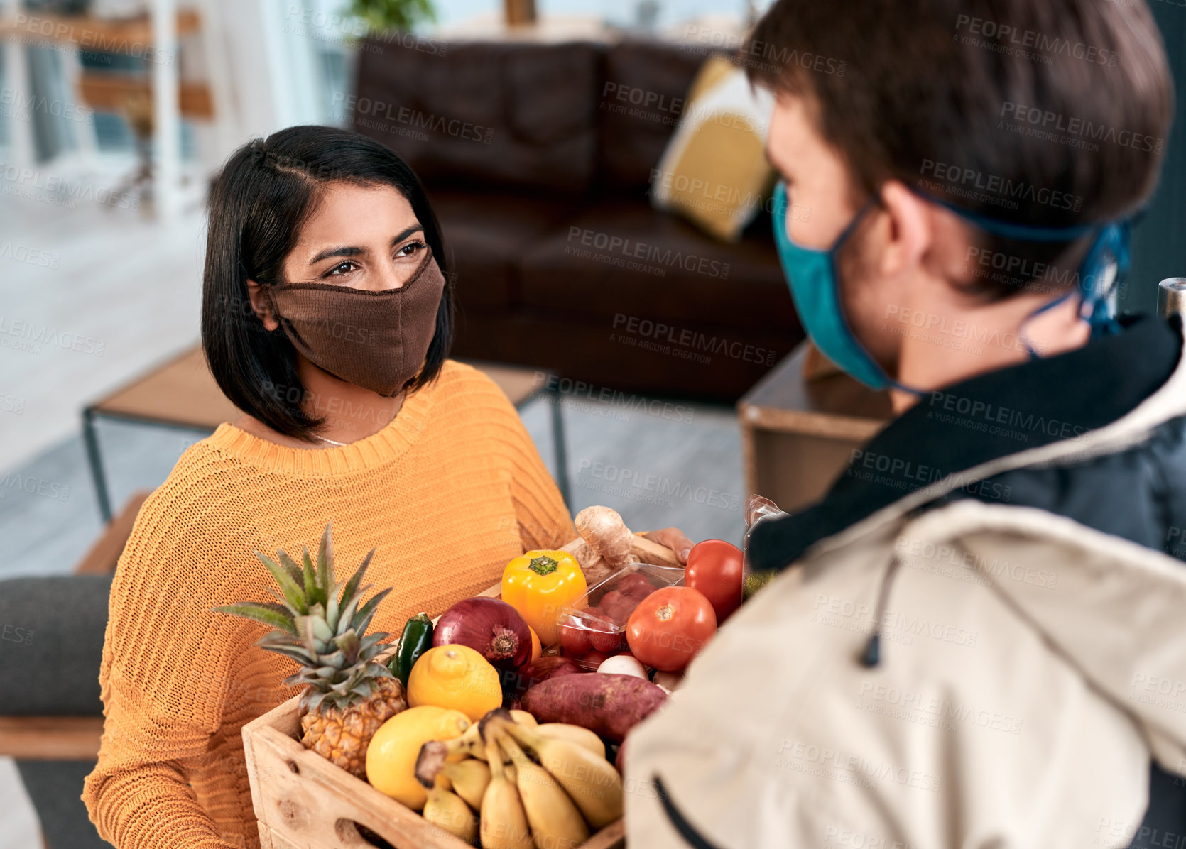 Buy stock photo Shot of a masked young woman receiving a delivery of fresh fruit and vegetables at home