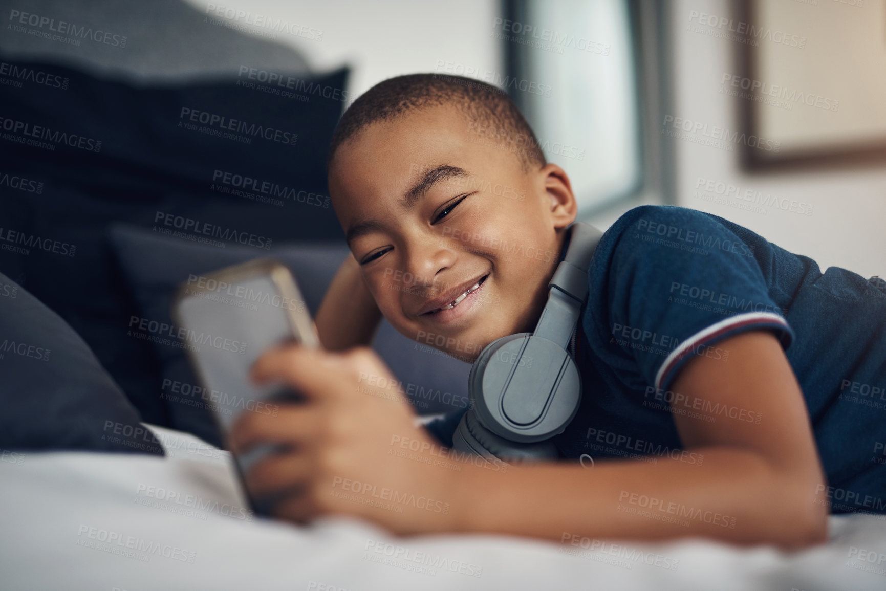 Buy stock photo Shot of a young boy using a cellphone while lying on his bed