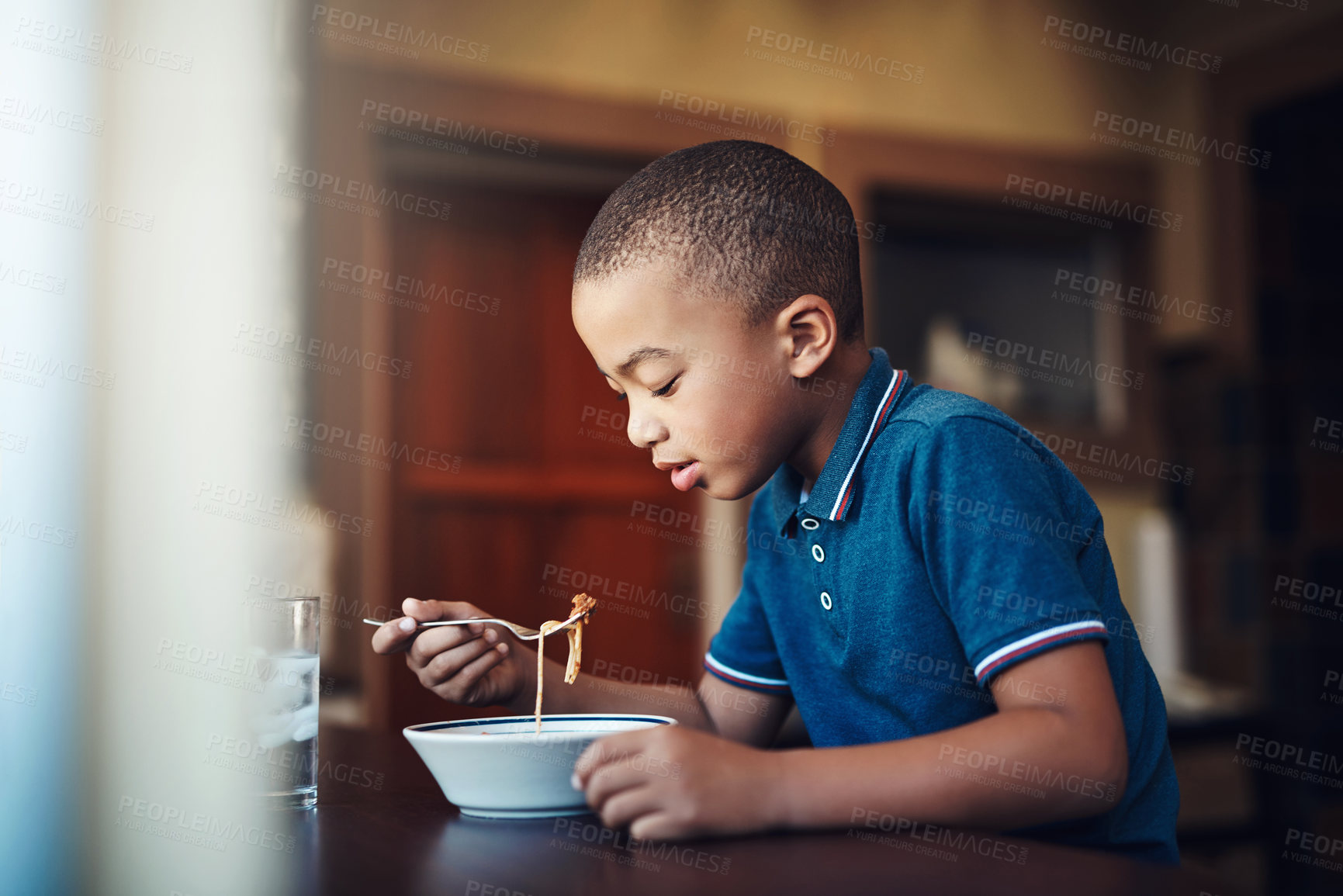 Buy stock photo Child, boy and eating pasta in home for nutrition, hungry and healthy development at table. African kid, food and spaghetti meal in house for lunch, dinner and cuisine with water at kitchen counter