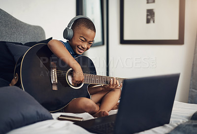 Buy stock photo Shot of a young boy wearing headphones while playing the guitar