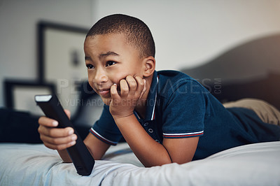 Buy stock photo Shot of a young boy using a remote control while lying on his bed