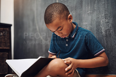 Buy stock photo Shot of a young boy writing in a book while sitting at home