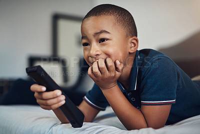 Buy stock photo Shot of a young boy using a remote control while lying on his bed