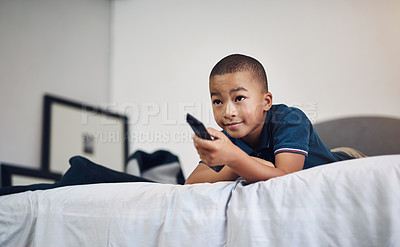 Buy stock photo Shot of a young boy using a remote control while lying on his bed