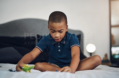 Buy stock photo Shot of a young boy playing with dinosaurs while sitting on his bed