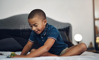 Buy stock photo Shot of a young boy playing with dinosaurs while sitting on his bed