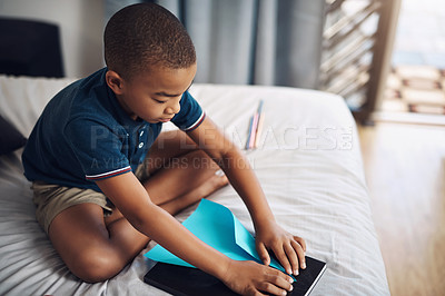 Buy stock photo Shot of a young boy making paper planes while sitting on his bed