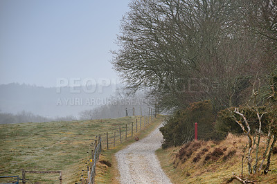 Buy stock photo A countryside dirt road leading to agriculture fields or farm pasture in remote area during early morning with fog or mist. Landscape view of quiet, scenery and mystical farming meadows in Germany