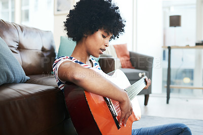 Buy stock photo Shot of a young woman playing the guitar while sitting at home