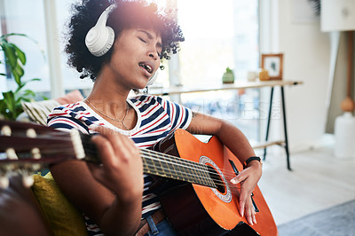 Buy stock photo Shot of a woman wearing headphones while playing the guitar at home