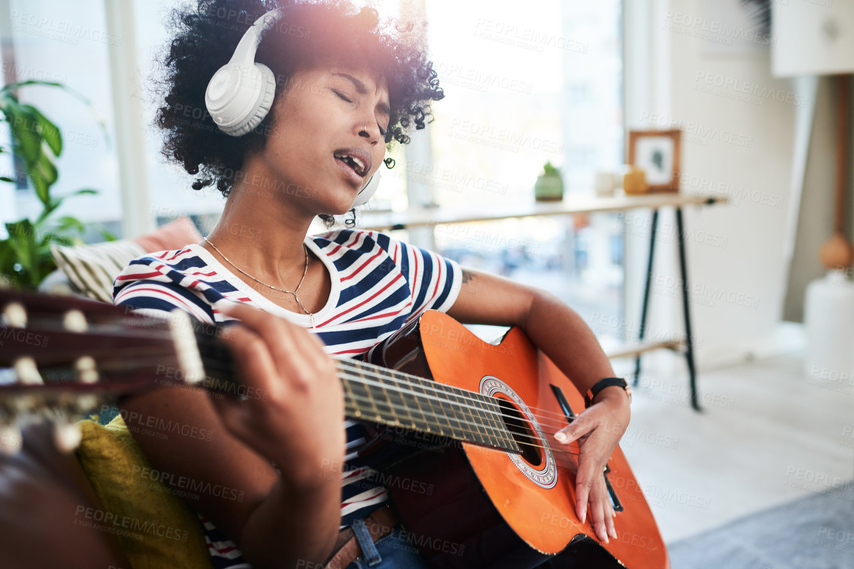 Buy stock photo Shot of a woman wearing headphones while playing the guitar at home