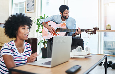 Buy stock photo Shot of a woman using her laptop while her boyfriend plays the guitar