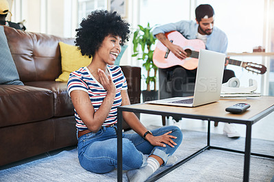 Buy stock photo Shot of a woman using her laptop while her boyfriend plays the guitar in the background