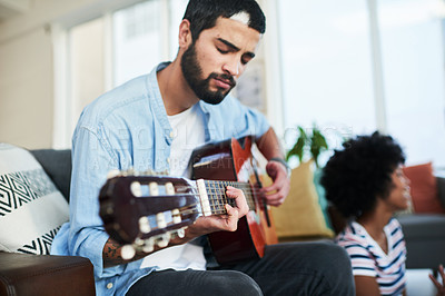 Buy stock photo Shot of a man playing the guitar while his girlfriend sits in the background