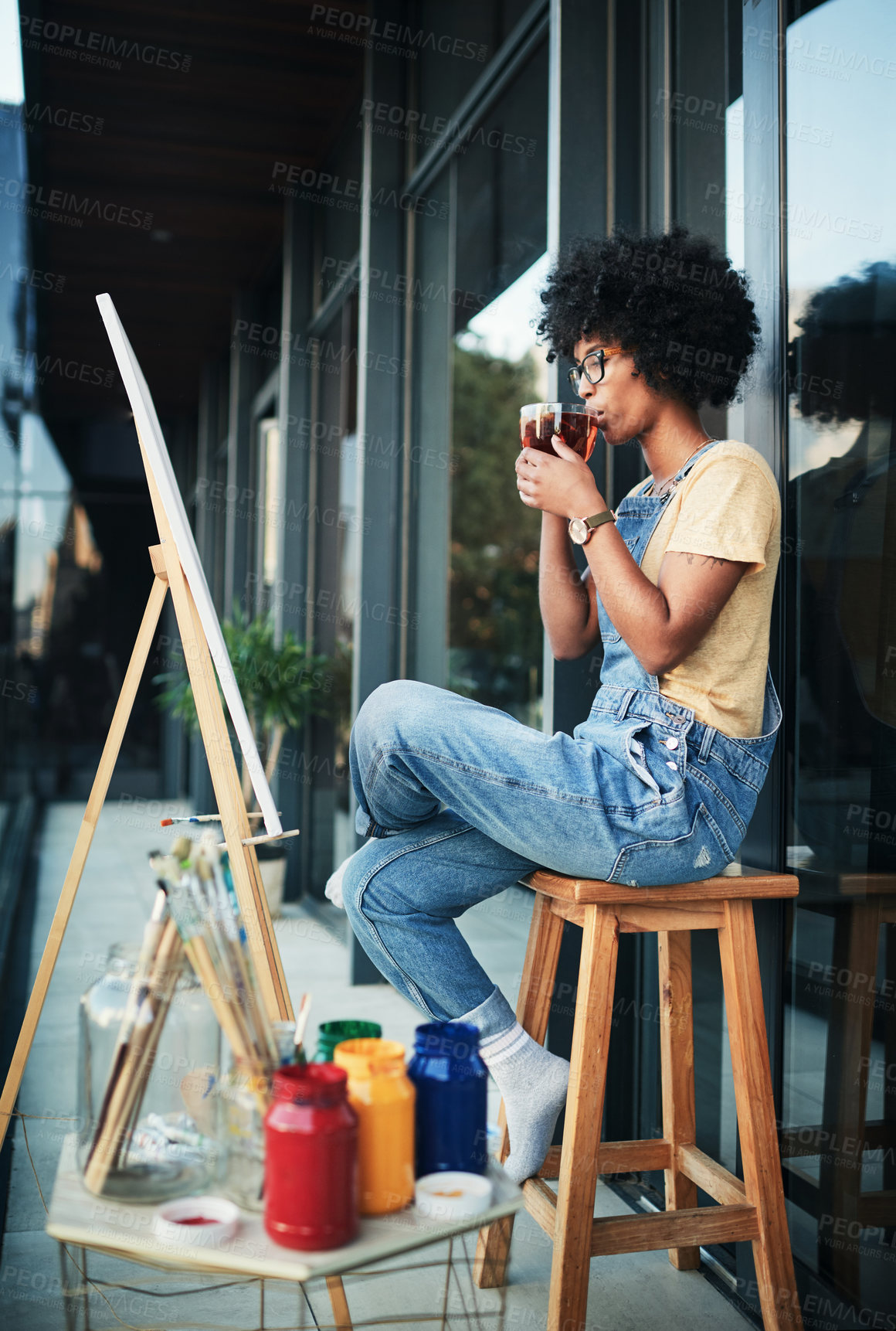 Buy stock photo Shot of a young artist having tea while sitting on the balcony with a canvas