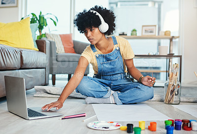 Buy stock photo Shot of a young woman using her laptop while sitting at home with paint and a blank canvas