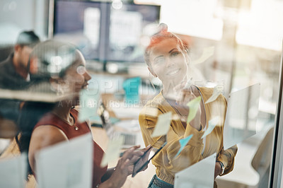 Buy stock photo Shot of two businesswomen brainstorming with notes on a glass wall in an office