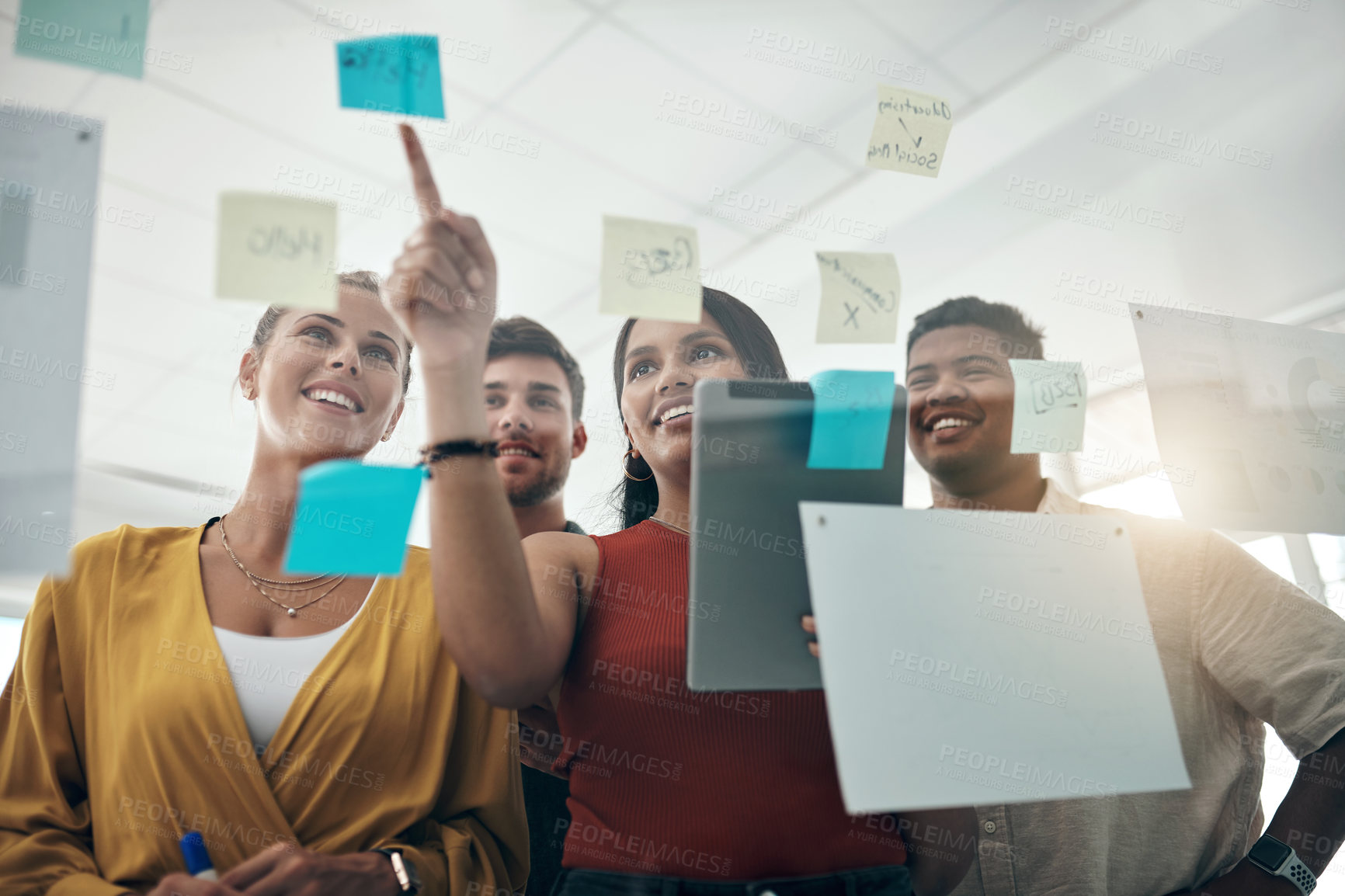 Buy stock photo Shot of a group of businesspeople using a digital tablet while brainstorming with notes on a glass wall in an office