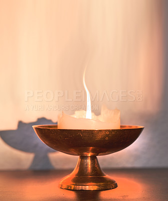 Buy stock photo Decor of golden dish with burning white candle that creates light, shadows and warmth by thin orange line of fire. Wax of object is half melted. A round and elegant bowl with a stand